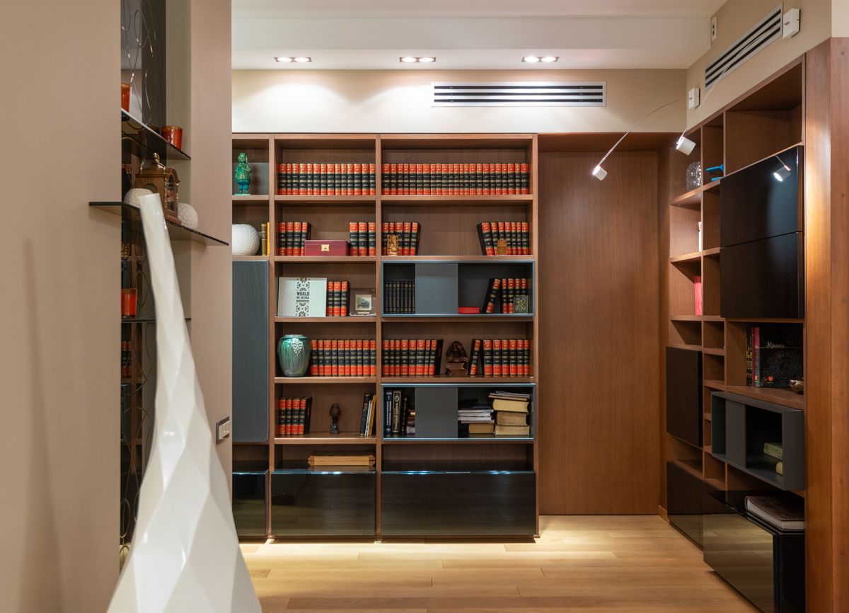 Wandfüllende Bücherregale aus mittelbraunem Holz mit geschlossenen und schwarzen Elementen